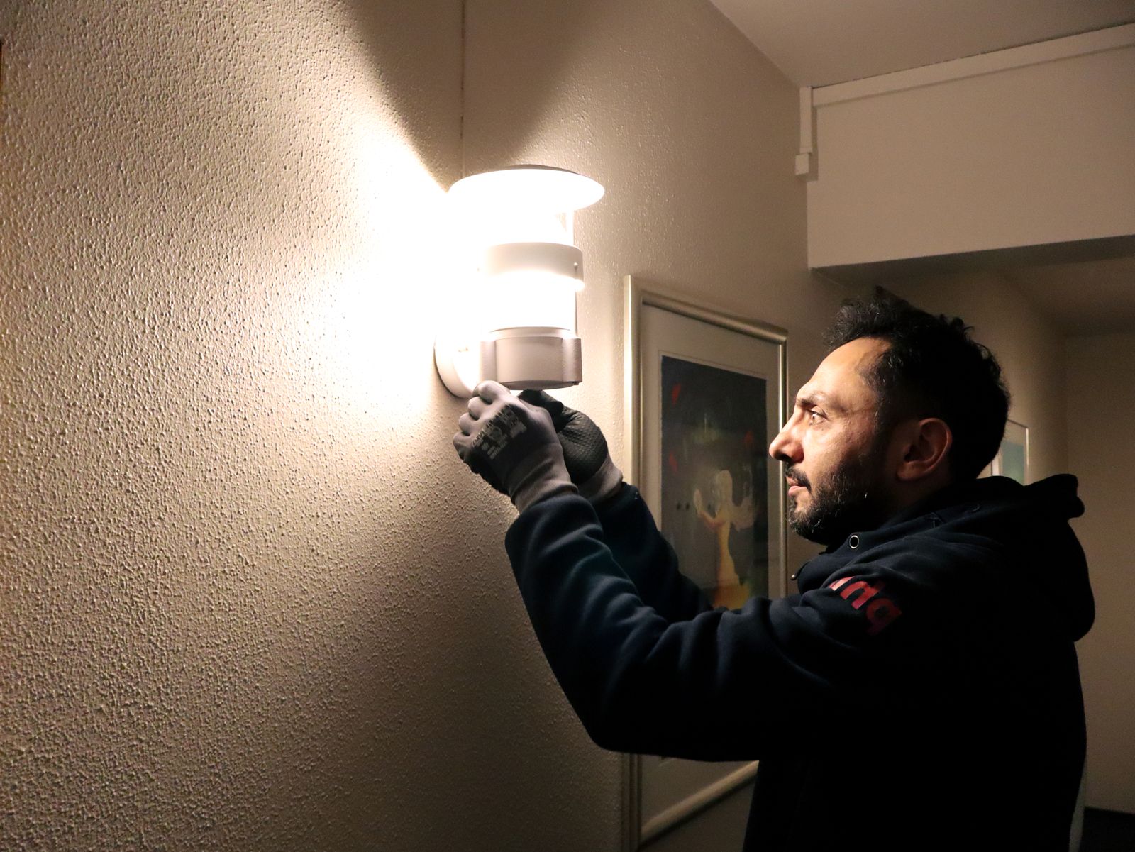 Vaktmester skifter lyspære i en vegglampe i fellesarealet, en del av våre vaktmestertjenester